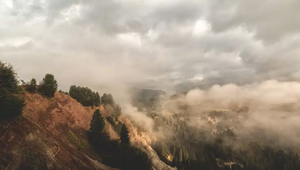 Mystische Berglandschaft mit Nebel und Wolken, die über bewaldete Hügel und steile Felsformationen ziehen – Symbol für die stille Schönheit und Mystik der Natur.