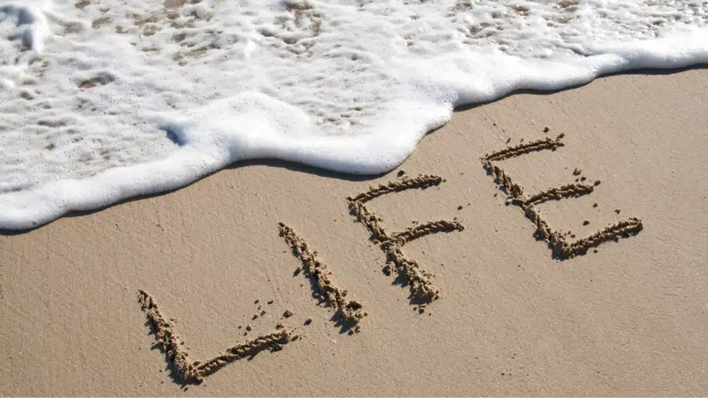 Wort Life im Sand am Strand mit Wellen als Symbol für Neuanfang und neues Leben mit 50