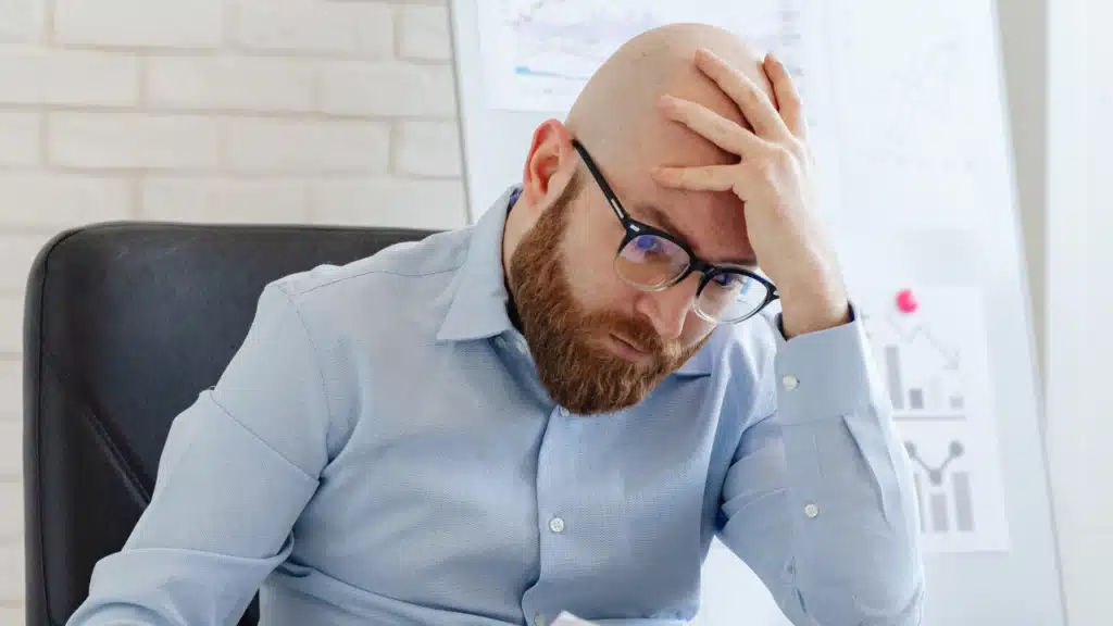 Ein gestresster Mann im Büro hält sich verzweifelt den Kopf – Symbol für Überlastung, Arbeitsdruck und die Herausforderungen im Berufsalltag.